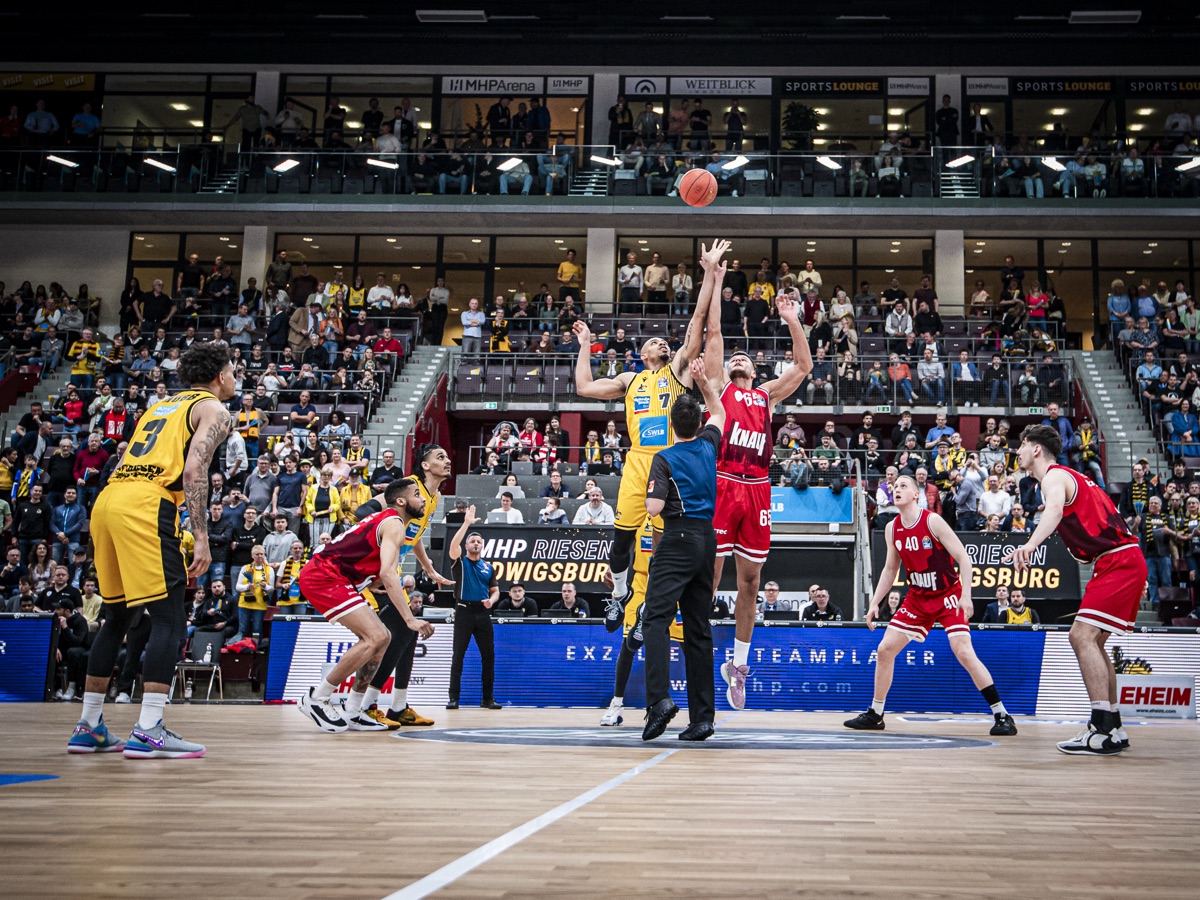 Sprungball in der MHPArena, Schiedsrichter und beide Teams, Ränge im Hintergrund